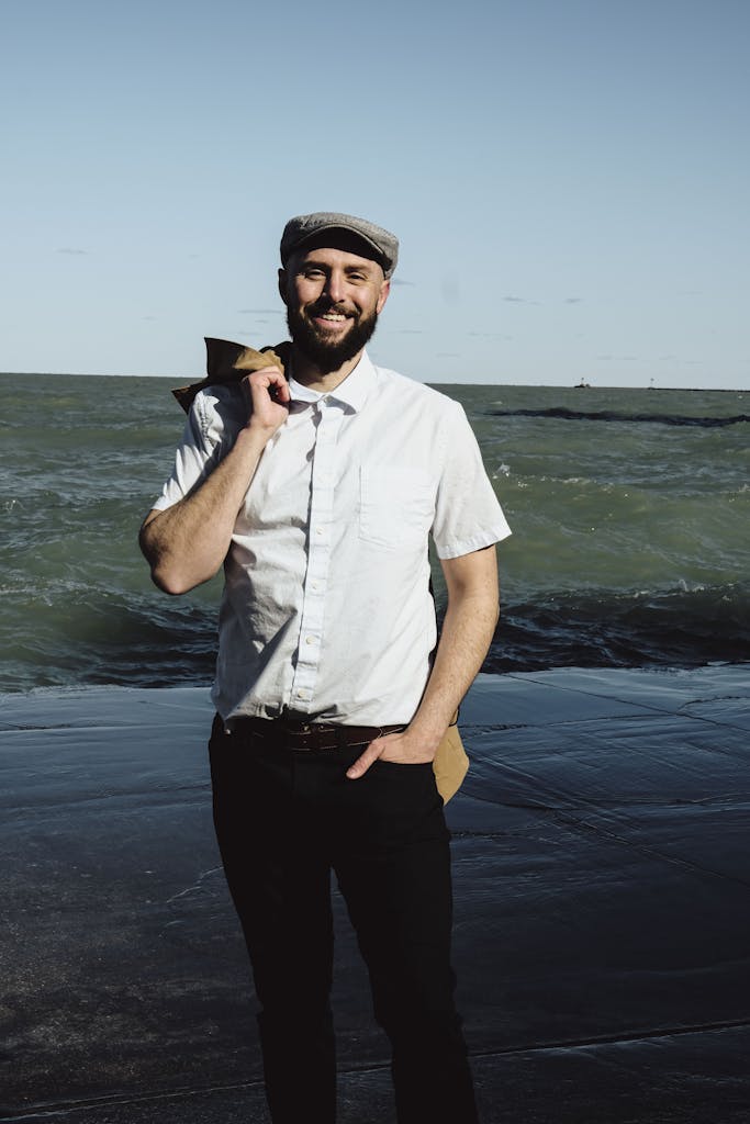 A man in a hat and shirt standing by the water